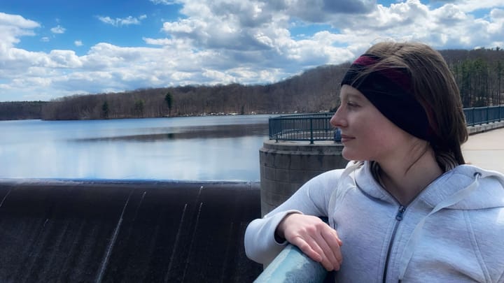 Clara Ritger gazes out over the waterfall of a dam on a sunny day.