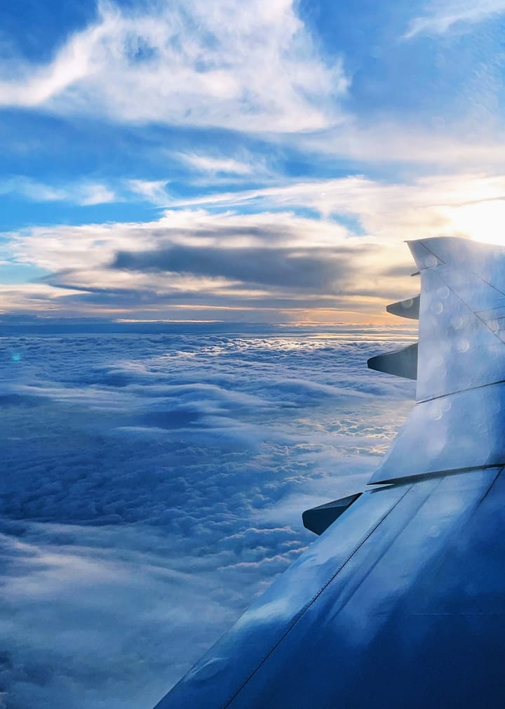 The wing of a plane in a blue sky with a yellow sun.