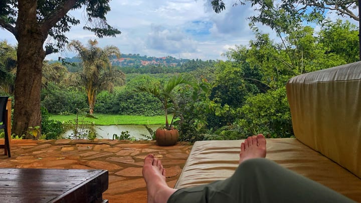 Feet lounging on a cushioned bench with a river and green jungle view in the distance.