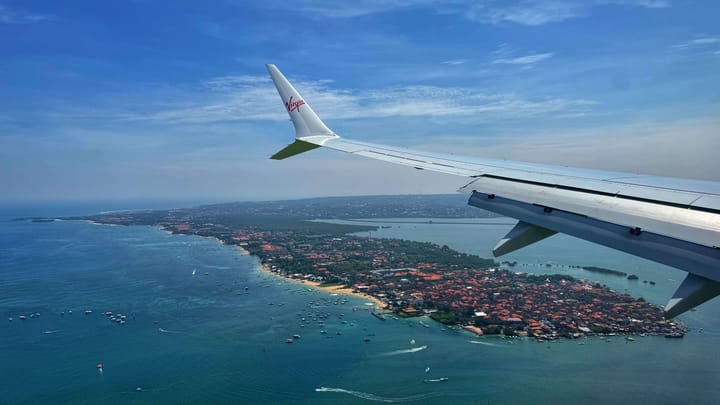An airplane view of an island in the ocean with boats on a clear blue day.