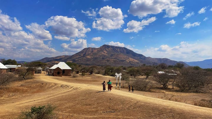 Two women and two children stand on a dusty road, with a mountain rising up behind them.