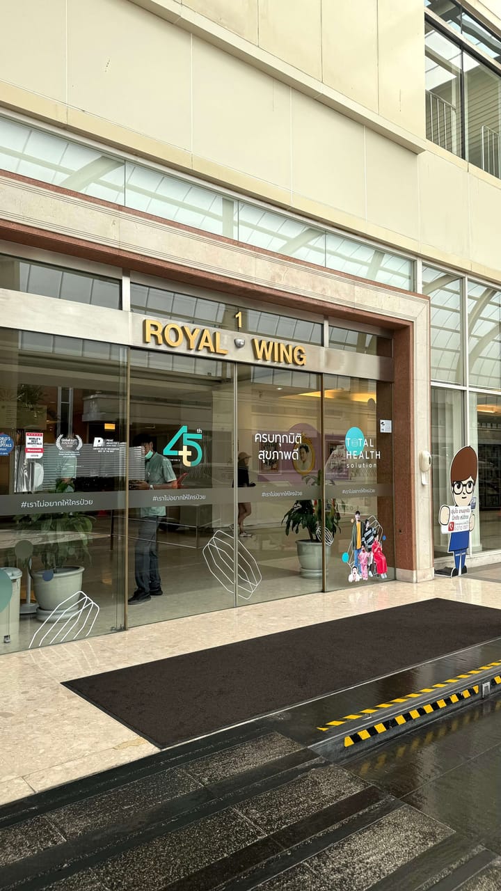 A beige and modern exterior entrance of a hospital, with sliding glass doors. 