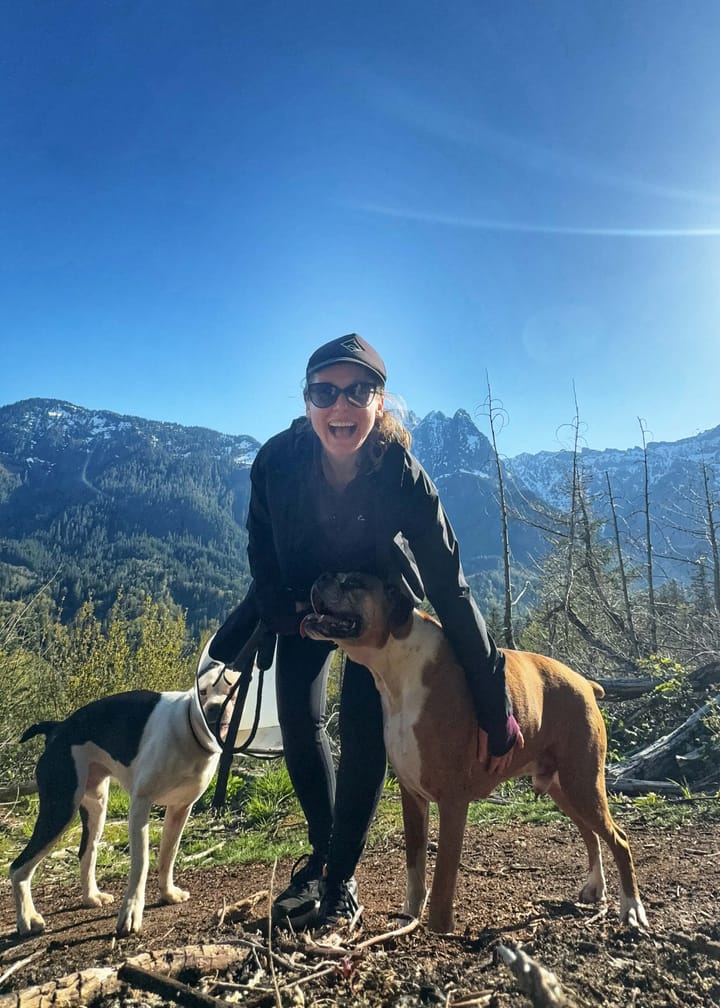 Clara Ritger smiles at the top of a mountain trail with two boxer dogs.