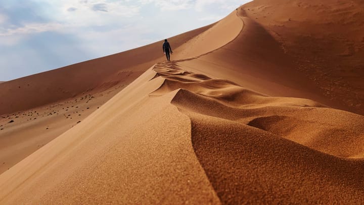 A person climbs a red sand dune.