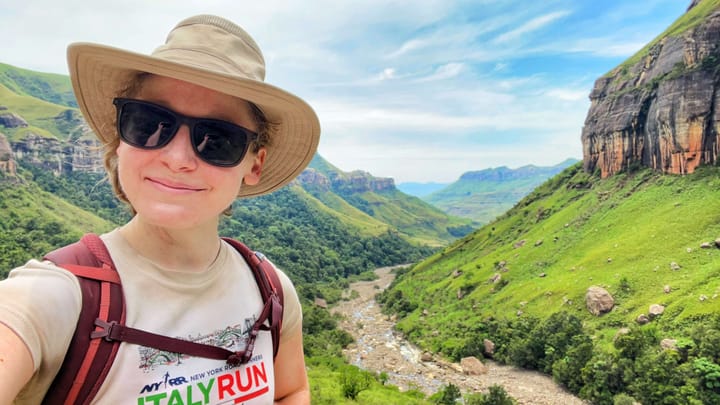 A woman smiles at the camera in front of a river cutting through a grassy canyon landscape.