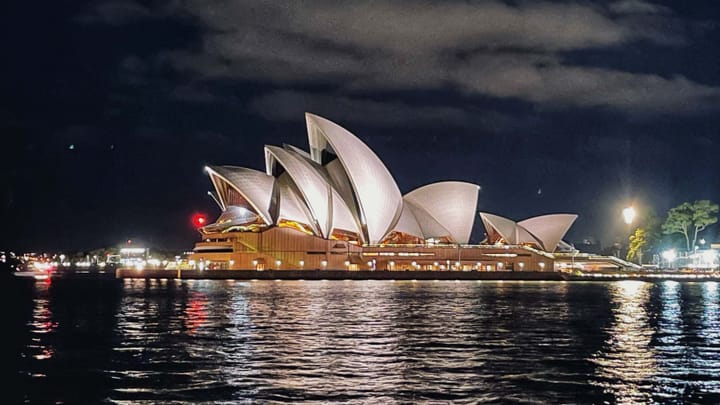 Along the waterfront in the night time, a building made of white, partial sphere shells. 