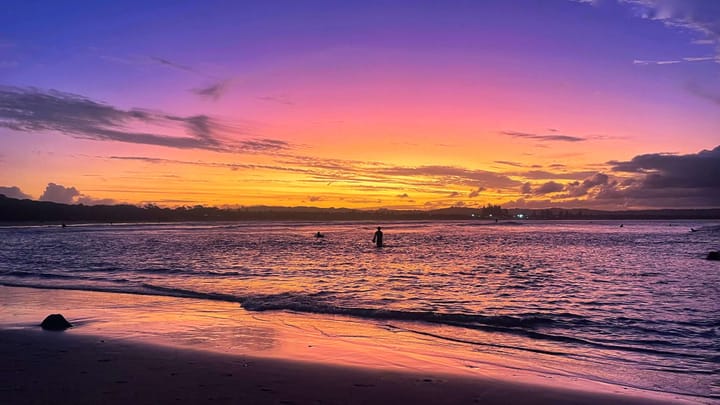 A purple, pink, and golden yellow dusk falls over the ocean.